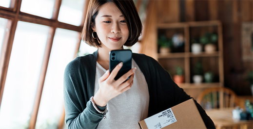 Woman looking at her phone while holding a small package.