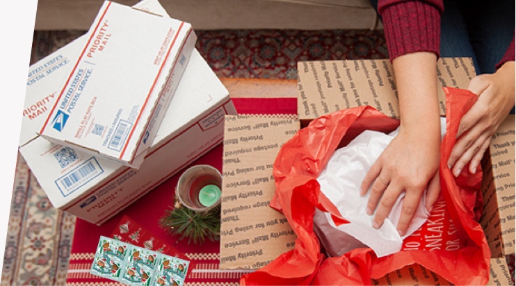 Young woman preparing holiday gifts and Priority Mail boxes to ship for December 25 delivery.