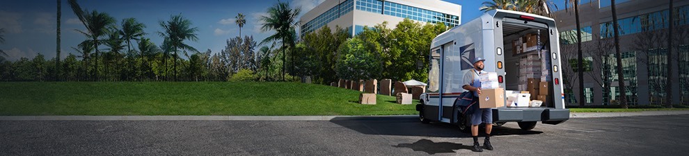 Letter carrier ready to deliver packages unloaded from the back of a USPS Next-Generation Delivery Vehicle.